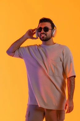 قضاء اوقات ممتعة بالاستماع الى الموسيقى، مفهوم الغناء والطرب، رجل يستخدم تقنية الهيدفون الحديثة، بورتريه لشاب اسمر عربي خليجي اماراتي مبتسم يرتدي الزي الكاجوال والنظارة الشمسية يمسك بيده سماعة الرأس بتعابير الفرح والسرور، خلفية برتقالي