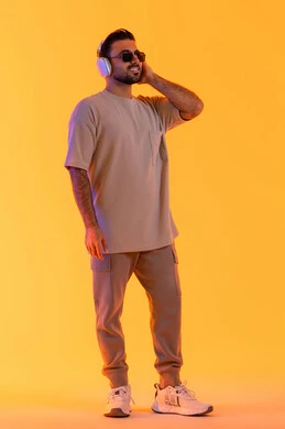 متابعة الموسيقى والترفيه بالهيدفون، اوقات ممتعة بالاستماع الى الموسيقى، مفهوم الغناء والطرب، رجل يستخدم تقنية الهيدفون الحديثة، بورتريه لشاب اسمر عربي خليجي اماراتي مبتسم يرتدي الزي الكاجوال والنظارة الشمسية يمسك بيده سماعة الرأس بتعابير الفرح والسرور، خلفية برتقالي
