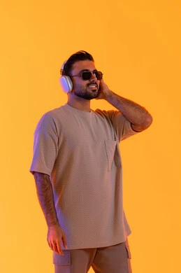 الموسيقى والترفيه بالهيدفون، اوقات ممتعة بالاستماع الى الموسيقى، مفهوم الغناء والطرب، رجل يستخدم تقنية الهيدفون الحديثة، بورتريه لشاب اسمر عربي خليجي اماراتي مبتسم يرتدي الزي الكاجوال والنظارة الشمسية يمسك بيده سماعة الرأس بتعابير الفرح والسرور، خلفية برتقالي