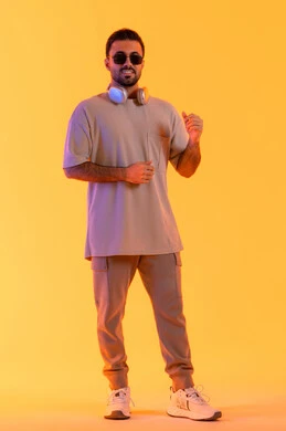 Dancing and interacting with music, enjoyable times listening to music, the concept of singing and melody, a man using modern technology, a portrait of a smiling young Arab Gulf Emirati man with a dark complexion wearing casual attire and sunglasses, wearing headphones with expressions of joy and happiness, orange background.