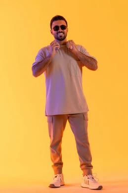 وجه مبتهج وابتسامة عريضة، اوقات ممتعة بالاستماع الى الموسيقى، مفهوم الغناء والطرب، رجل يستخدم التقنية الحديثة، بورتريه لشاب اسمر عربي خليجي اماراتي مبتسم يرتدي الزي الكاجوال والنظارة الشمسية يضع سماعة الرأس بتعابير الفرح والسرور، خلفية برتقالي