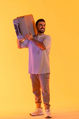 النظر بإيماءات السرور والسعادة، التحضير قضاء رحلة صيفية ممتعة، القيام بالجولات الترفيهية، مفهوم السياحة في إجازة الصيف، بورتريه لرجل عربي خليجي اماراتي يرتدي الزي الكاجوال  يحمل على كتفه حقيبة الامتعة، السياحة في إجازة الصيف, خلفية برتقاليه