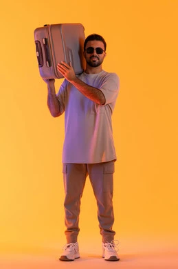 مفهوم السياحة في إجازة الصيف، ايماءات السرور والفرح، التحضير قضاء رحلة صيفية ممتعة، القيام بالجولات الترفيهية، بورتريه لرجل عربي خليجي اماراتي يرتدي الزي الكاجوال ونظارة شمسية يحمل على كتفه حقيبة الامتعة، السياحة في إجازة الصيف, خلفية برتقاليه