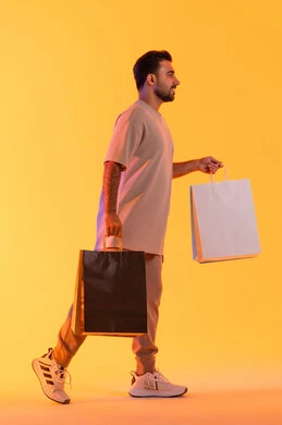 Gestures of joy and happiness, purchasing products and paying remotely, benefiting from offers and discounts, shopping and buying necessities and gifts, a side portrait of a smiling Emirati Gulf Arab man wearing casual attire holding paper bags in his hands, promoting products and global brands, orange background.