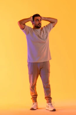 التفاجأ والاستغراب من شيء ما، مفهوم الرجولة والاناقة الخارجي، تعابير النجاح وتحقيق الأهداف, النظر إلى الكاميرا بإيماءات التعجب والدهشة، بورتريه لشاب عربي خليجي إماراتي يرتدي الزي الكاجوال يضع يديه خلف رأسه يشعر بالصدمة والذهول والانبهار، خلفية برتقاليه