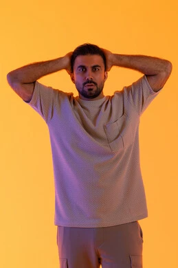 الاستغراب والتفاجأ من شيء ما، مفهوم الرجولة والاناقة الخارجي، تعابير النجاح وتحقيق الأهداف, النظر إلى الكاميرا بإيماءات التعجب والدهشة، بورتريه لشاب عربي خليجي إماراتي يرتدي الزي الكاجوال يضع يديه خلف رأسه يشعر بالصدمة والذهول والانبهار، خلفية برتقاليه