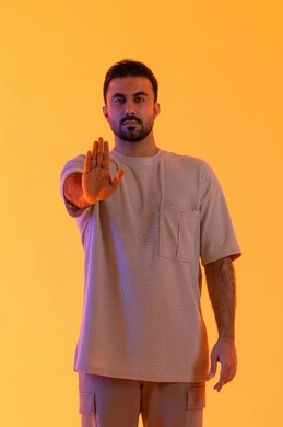 طلب التوقف عن فعل شيء ما، الأمر بالوقوف وعدم التمادي، الرفض وعدم الخضوع، النهي عن التقدم وأهمية ترك مسافة أمان، بورتريه لرجل عربي خليجي اماراتي يرتدي الزي الكاجوال يرفع كفه للأعلى، الاهتمام بالمظهر الخارجي، خلفية برتقاليه