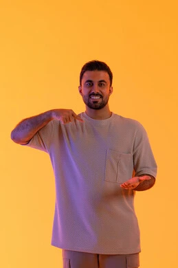 رفع وحمل شيء ما، الوقوف باستقامة واعتدال, النظر إلى الكاميرا بإيماءات السرور،مفهوم الوسامة والثقة بالنفس، بورتريه لرجل عربي خليجي اماراتي مبتسم يرتدي الزي الكاجوال يشير باصبع السبابة على يده، تعابير حمل عنصر، مفهوم الرجولة والاناقة، خلفية برتقاليه