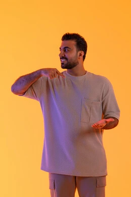 مفهوم الوسامة والثقة بالنفس، رفع وحمل شيء ما، الوقوف باستقامة واعتدال, النظر إلى الكاميرا بإيماءات السرور، بورتريه لرجل عربي خليجي اماراتي مبتسم يرتدي الزي الكاجوال يشير باصبع السبابة على يده، تعابير حمل عنصر، مفهوم الرجولة والاناقة، خلفية برتقاليه