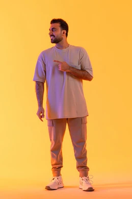 الإشارة إلى شيء ما, مفهوم الوسامة والثقة بالنفس، الوقوف باستقامة واعتدال, النظر إلى الكاميرا بإيماءات السرور، بورتريه لرجل عربي خليجي اماراتي مبتسم يرتدي الزي الكاجوال يشير باصبع ، تعابير حمل عنصر، مفهوم الرجولة والاناقة، الجسم بالطول الكامل، خلفية برتقاليه