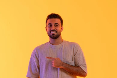 إشارات وحركات يدين تدل على هذا المكان،  مفهوم الوسامة والثقة بالنفس، الوقوف باستقامة واعتدال, النظر بإيماءات السرور، بورتريه لرجل عربي خليجي اماراتي مبتسم يرتدي الزي الكاجوال يشير بيديه لمكان معين، مفهوم الرجولة والاناقة، الإشارة إلى هدف محدد، خلفية برتقاليه