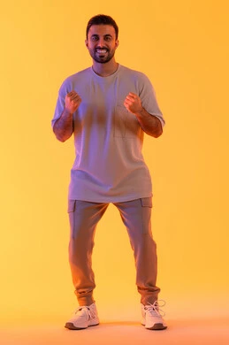 تعابير التفاعل والإندماج, بورتريه لشاب عربي خليجي إماراتي يرتدي الزي الكاجوال يرفع يديه مضموم الكفين, رجل سعودي ينظر بإيماءات السعادة والفوز والإنتصار, الشعور بالقوة والنجاح، أندية وتشجيع الفريق المفضل، الطول الكامل للجسم، خلفية صفراء
