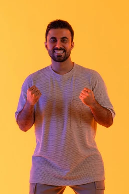 الشعور بالقوة والنجاح، تعابير التفاعل والإندماج, بورتريه لشاب عربي خليجي إماراتي يرتدي الزي الكاجوال يرفع يديه مضموم الكفين, رجل سعودي ينظر بإيماءات السعادة والفوز والإنتصار, أندية وتشجيع الفريق المفضل، خلفية صفراء