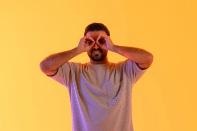 مفهوم التخطيط المستقبلي للأهداف والطموحات، حب المغامرة والاستكشاف، بورتريه مقرب لشاب عربي خليجي  اماراتي يرتدي الزي الكاجوال يضع يده على عينه على شكل منظار، رجل سعودي يقوم برؤية الاشياء البعيدة، خلفية صفراء