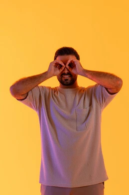 التخطيط المستقبلي للأهداف والطموحات، حب المغامرة والاستكشاف، بورتريه لشاب عربي خليجي  اماراتي يرتدي الزي الكاجوال يضع يده على عينه على شكل منظار، رجل سعودي يقوم برؤية الاشياء البعيدة، خلفية صفراء