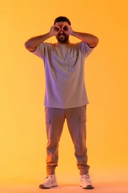 حب المغامرة والاستكشاف، التخطيط المستقبلي للأهداف والطموحات، بورتريه لشاب عربي خليجي  اماراتي يرتدي الزي الكاجوال يضع يده على عينه على شكل منظار، رجل سعودي يقوم برؤية الاشياء البعيدة، الجسم بالطول الكامل، خلفية صفراء