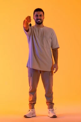 Receiving and delivering keys, obtaining a driver's license, the excitement of owning a new car, valet parking service, a portrait of a young Arab Gulf Emirati man wearing casual attire holding a key in his hand, full-body, yellow background.