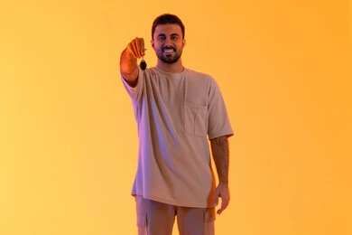 The excitement of owning a new car, receiving and handing over the keys, obtaining a driver's license, valet parking service, a Saudi man looking at the camera with expressions of joy, a portrait of a young Arab Gulf Emirati wearing casual attire holding a key in his hand, full-body, yellow background.