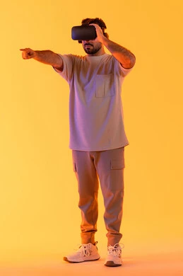 الاشارة بإصبع السبابة إلى شيء ما، استخدام الأجهزة التقنية في رؤية المشاهد الخيالية، التفاعل والاندماج مع الواقع الافتراضي، بورتريه لشاب عربي خليجي إماراتي يرتدي الزي الكاجوال يضع نظارات الفي آر، رجل سعودي يقضي أوقات الفراغ بشكل ممتع، الطول الكامل للجسم، خلفية صفراء