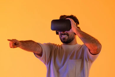 رؤية المشاهد الخيالية، الاشارة بإصبع السبابة إلى شيء ما، استخدام الأجهزة التقنية الحديثة، التفاعل والاندماج مع الواقع الافتراضي، بورتريه مقرب لشاب عربي خليجي إماراتي يرتدي الزي الكاجوال يضع نظارات الفي آر، رجل سعودي يقضي أوقات الفراغ بشكل ممتع، خلفية صفراء