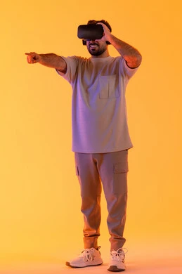 الاشارة بإصبع السبابة إلى شيء ما، استخدام الأجهزة التقنية في رؤية المشاهد الخيالية، التفاعل والاندماج مع الواقع الافتراضي، بورتريه لشاب عربي خليجي إماراتي يرتدي الزي الكاجوال يضع نظارات الفي آر، رجل سعودي يقضي أوقات الفراغ بشكل ممتع، الطول الكامل للجسم، خلفية صفراء