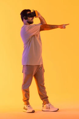الاشارة بإصبع السبابة إلى شيء ما، استخدام الأجهزة التقنية في رؤية المشاهد الخيالية، التفاعل والاندماج مع الواقع الافتراضي، بورتريه لشاب عربي خليجي إماراتي يرتدي الزي الكاجوال يضع نظارات الفي آر، رجل سعودي يقضي أوقات الفراغ بشكل ممتع، الطول الكامل للجسم، خلفية صفراء
