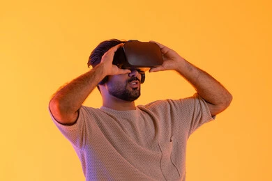 السرور و السعادة برؤية المشاهد الخيالية، استخدام الأجهزة التقنية الحديثة، التفاعل والاندماج مع الواقع الافتراضي، بورتريه مقرب لشاب عربي خليجي إماراتي يرتدي الزي الكاجوال يضع نظارات الفي آر، رجل سعودي يقضي أوقات الفراغ بشكل ممتع، خلفية صفراء