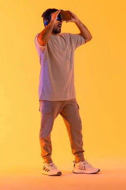 التفاعل والاندماج مع الواقع الافتراضي، بورتريه لشاب عربي خليجي إماراتي يرتدي الزي الكاجوال يضع نظارات الفي آر، استخدام الأجهزة التقنية الحديثة والتكنولوجيا في رؤية المشاهد الخيالية، رجل سعودي يقضي أوقات الفراغ بشكل ممتع، الطول الكامل للجسم، خلفية صفراء