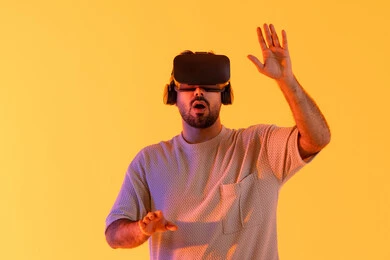 السرور و السعادة برؤية المشاهد الخيالية، استخدام الأجهزة التقنية الحديثة، التفاعل والاندماج مع الواقع الافتراضي، بورتريه مقرب لشاب عربي خليجي إماراتي يرتدي الزي الكاجوال يضع نظارات الفي آر، رجل سعودي يقضي أوقات الفراغ بشكل ممتع، خلفية صفراء