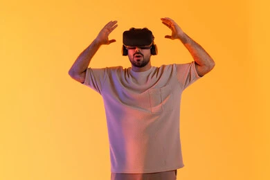 Simulation of the imaginary world, happiness in seeing imaginary scenes, using modern technological devices, interaction and immersion with virtual reality, a portrait of a young Emirati Arab man wearing casual attire and VR glasses, a Saudi man enjoying his leisure time, yellow background.