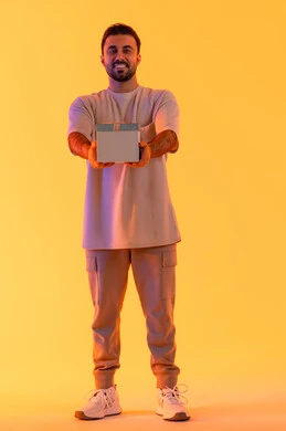 التعبير عن الحب والتقدير والاحترام، تقديم الهدايا بالاعياد والمناسبات الخاصة، مفهوم الشكر والامتنان، رجل سعودي ينظر إلى الكاميرا بايماءات الفرح والسرور، بورتريه لشاب عربي خليجي اماراتي يرتدي الزي الكاجوال يحمل بيديه صندوق هدية، الجسم بالطول الكامل، خلفية صفراء