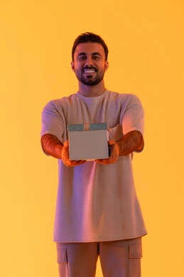The concept of gratitude and appreciation, expressing love, respect, and admiration, giving gifts during holidays and special occasions, a Saudi man looking at the camera with gestures of joy and happiness, a portrait of a young Emirati Arab man wearing casual attire holding a gift box in his hands, with a yellow background.