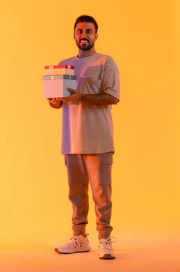Expressing love, appreciation, and respect, giving gifts on holidays and special occasions, the concept of thanks and gratitude, a Saudi man looking at the camera with gestures of joy and happiness, a portrait of a young Arab Gulf Emirati man wearing casual attire holding a gift box in his hands, full-body, yellow background.