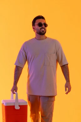 السياحة في إحدى منتجعات الإمارات, الاستمتاع بالمشروبات الباردة وقضاء وقت ممتع في العطلة الصيفية, بورتريه لشاب عربي خليجي سعودي مبتسم يرتدي الزي الكاجوال والنظارة الشمسية، رجل اماراتي يحمل حافظة العصائر وينظر إلى شيء ما, خلفية صفراء