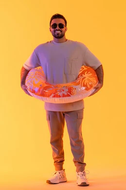 الاستمتاع في شواطئ الامارات بإيماءات البشاشة والسرور, قضاء أوقات صيفية سياحية, التسلية في إحدى المنتجعات الترفيهيه, بورتريه لشاب عربي خليجي سعودي مبتسم يرتدي الزي الكاجوال والنظارة، رجل اماراتي يرتدي عوامة السباحة, الجسم بالطول الكامل, خلفية صفرء