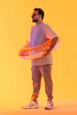 Enjoying the beaches of the UAE with gestures of cheerfulness and joy, spending summer tourist times, having fun at one of the entertainment resorts, a portrait of a smiling young Arab Gulf Saudi man wearing casual attire and glasses, an Emirati man wearing a swimming float, full body, yellow background.