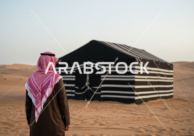 مخيمات سياحية في المناطق البرية، كشتة و جلسة بر شبابية، التخييم في صحاري السعودية، صورة من الخلف لرجل عربي خليجي سعودي يرتدي الثوب والشماغ التقليدي في خيمة بدوية شعبية وسط الصحراء، الأجواء الشتوية الهادئة