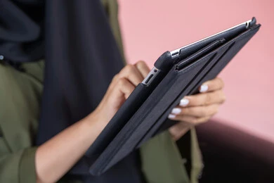 دمج التكنولوجيا الحديثة في الحياة اليومية والعملية، استخدام خاصية اللمس ، ايماءات يدين بالنقر بالاصبع على الشاشة، استخدام اجهزة تقنية حديثة، بورتريه مقرب  من الجانب ليد شابة عربية خليجية اماراتية  تحمل جهاز التابلت، خلفية وردية