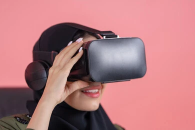 الاستمتاع بمشاهدة أفلام الواقع الافتراضي، التفاعل والاندماج ومحاكاة العالم الخيالي, بورتريه مقرب لامرأة اماراتية عربية خليجية محجبة ترتدي العباءة ونظارة في آر ثلاثية الأبعاد تنظر إلى شيء ما بتركيز, الترفيه والتسلية في وقت الفراغ, خلفية وردية