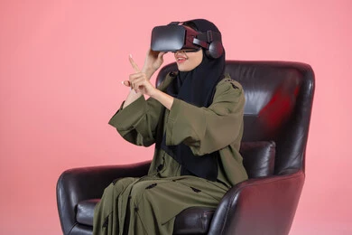 An attempt to touch something, gestures of interaction and integration, the concept of modern electronic technologies, a close-up portrait of an Emirati Arab Gulf woman wearing a hijab and an abaya, with 3D virtual reality (VR) glasses sitting on a chair clicking on something, colorful background. An attempt to touch something, gestures of interaction and integration, the concept of modern electronic technologies, a close-up portrait of an Emirati Arab Gulf woman wearing a hijab and an abaya, with 3D virtual reality (VR) glasses sitting on a chair clicking on something, colorful background.
