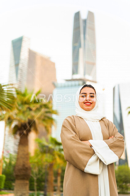 سيدة عربية خليجية سعودية تقف مكتفة اليدين امام ابراج مدينة الملك عبد الله المالية كافد في مدينة الرياض في المملكة العربية السعودية ، قضاء وقت ممتع ، جولة سياحية في المدينة المالية