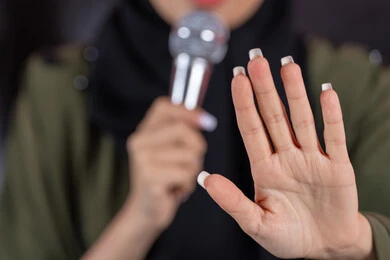 مفهوم الفن وتأثيره الايجابي، تقديم العروض الفنيه و الغنائيه والفقرات الترفيهية، بورترية مقرب ليد امراة عربيه خليجيه اماراتية تمسك بيديها الميكروفون ترفع يديها للاعلي بايماءات الامر بالتوقف عن فعل شيء ما، خلفية وردية
