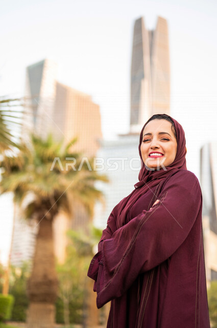 سيدة عربية خليجية سعودية تقف مكتفة اليدين امام ابراج مدينة الملك عبد الله المالية كافد في مدينة الرياض في المملكة العربية السعودية ، قضاء وقت ممتع ، جولة سياحية في المدينة المالية
