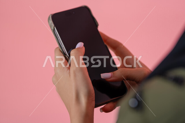 عرض شاشة الجوال, بورتريه مقرب ليد امرأة عربية خليجية اماراتية  تحمل الهاتف المحمول، استعمال التكنولوجيا الحديثة في انجاز المهام عن بعد، الاستفادة من خدمات وتطبيقات الموبايل، الدردشه مع الأهل والأصدقاء، خلفية وردية
