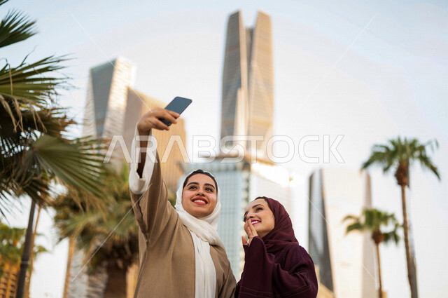 Two Saudi Arabian Gulf women are taking a selfie at King Abdullah Financial District, Kafed, in Riyadh, Kingdom of Saudi Arabia ,meeting and acquaintance, making friends, sightseeing tour, spending quality time in the financial city