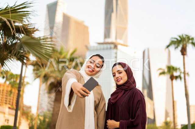Two Saudi Arabian Gulf women are taking a selfie at King Abdullah Financial District, Kafed, in Riyadh, Kingdom of Saudi Arabia ,meeting and acquaintance, making friends, sightseeing tour, spending quality time in the financial city