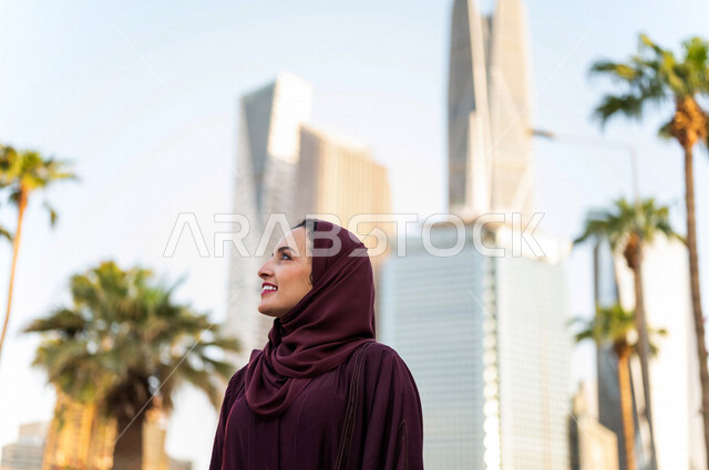 سيدة عربية خليجية سعودية تقف امام ابراج مدينة الملك عبد الله المالية كافد في مدينة الرياض في المملكة العربية السعودية ، قضاء وقت ممتع ، جولة سياحية في المدينة المالية