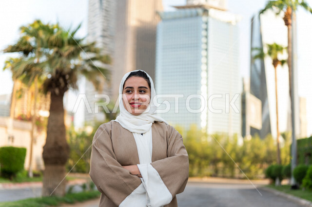 سيدة عربية خليجية سعودية تقف مكتفة اليدين امام ابراج مدينة الملك عبد الله المالية كافد في مدينة الرياض في المملكة العربية السعودية ، قضاء وقت ممتع ، جولة سياحية في المدينة المالية