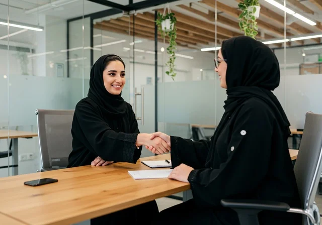 Successful new business deals between businesswomen, friendships and networking, and building social relationships among employees, partnerships in business and projects, two Arab Gulf Saudi women shaking hands, expanding work fields, office jobs and professions for women.