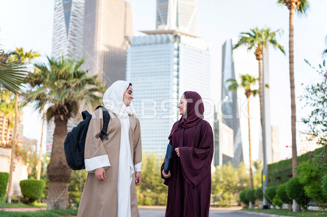 سيدة اعمال عربية خليجية سعودية تحمل بيدها الحاسوب المحمول تتحدث مع سيدة خليجية سعودية ، التجول في مدينة الملك عبد الله المالية كافد في مدينة الرياض في المملكة العربية السعودية ،قضاء وقت ممتع في المدينة المالية